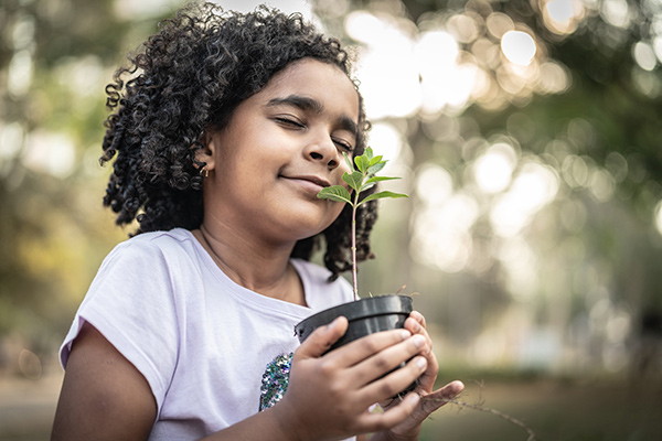Little Girl in garden, smelling fresh plant - Learn more about sustainable gains