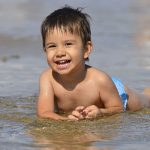 Child laying on beach in water - find out everything you need to know about SPF boosters in sunscreen formulations in the Prospector Knowledge Center.