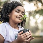 Little Girl in garden, smelling fresh plant - Learn more about sustainable gains